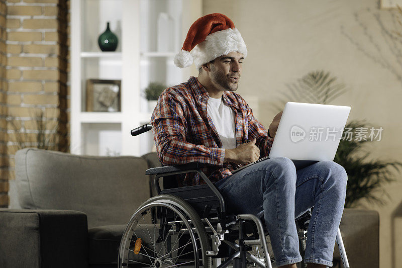 一个年轻人坐在轮椅上与圣诞老人的帽子在一个视频电话祝愿圣诞股票照片快乐