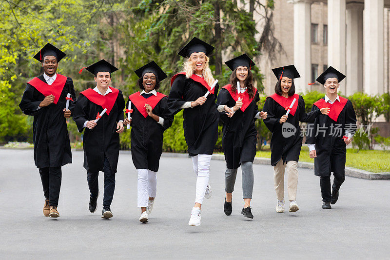 身着毕业服装在大学校园里奔跑的多种族学生们欣喜不已