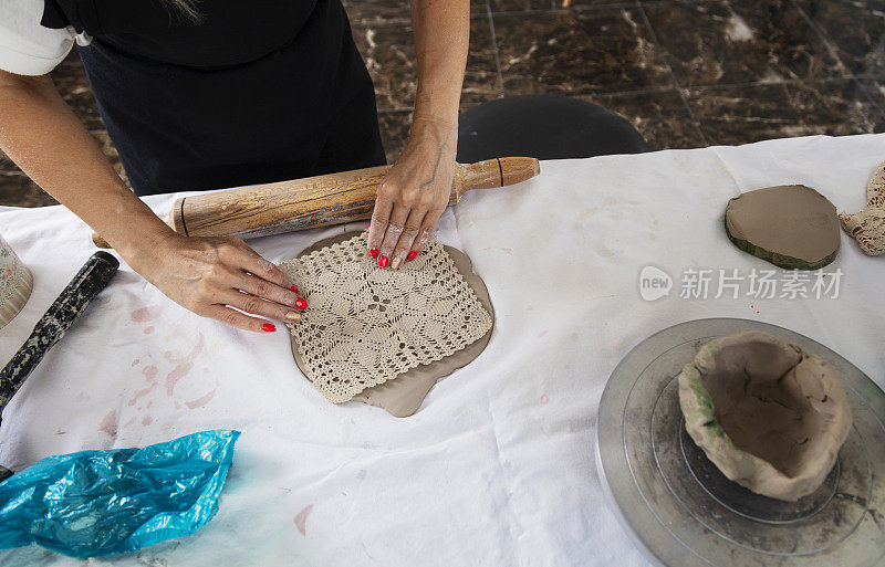 陶瓷艺术家在用擀面针压平粘土泥后用蕾丝样品塑造粘土。