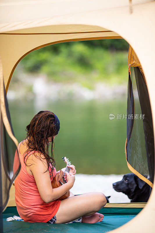 一个女人和狗在帐篷里玩尤克里里琴