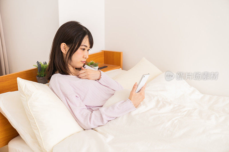 漂亮的亚洲女人在床上用智能手机，想想