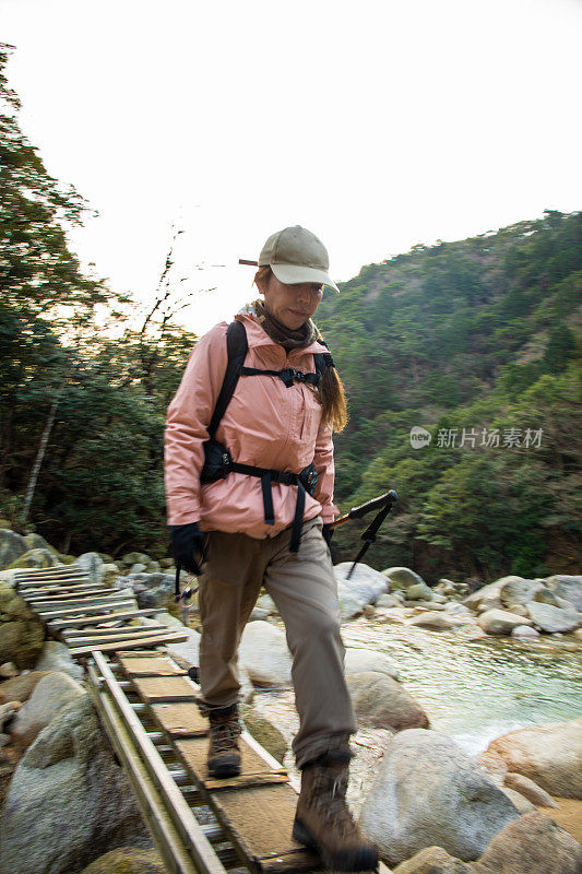 一位女登山客穿过小溪上的木桥