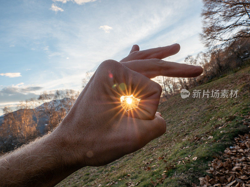 手捕捉阳光的细节，背景上的山