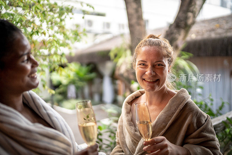 快乐的女人穿着浴袍，在温泉里喝香槟的肖像