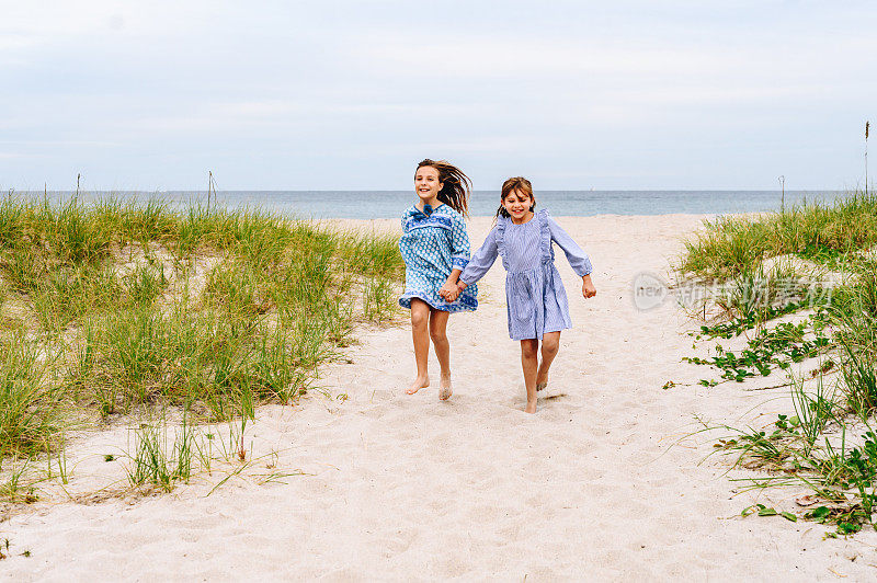 快乐的女孩牵着手在田园诗般的海滩上奔跑，孩子们在度假