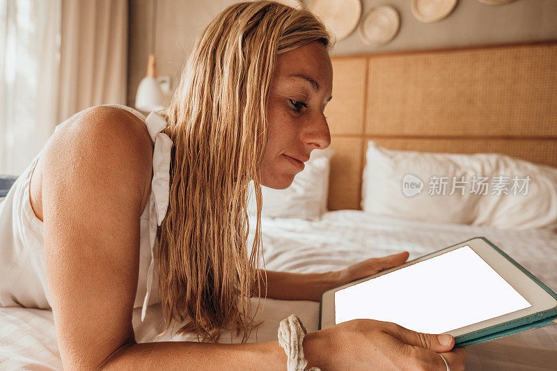 年轻女子在她舒适的床上使用数码平板电脑-早上好