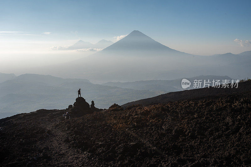 危地马拉，一名男子站在两座火山前的一块火山岩上