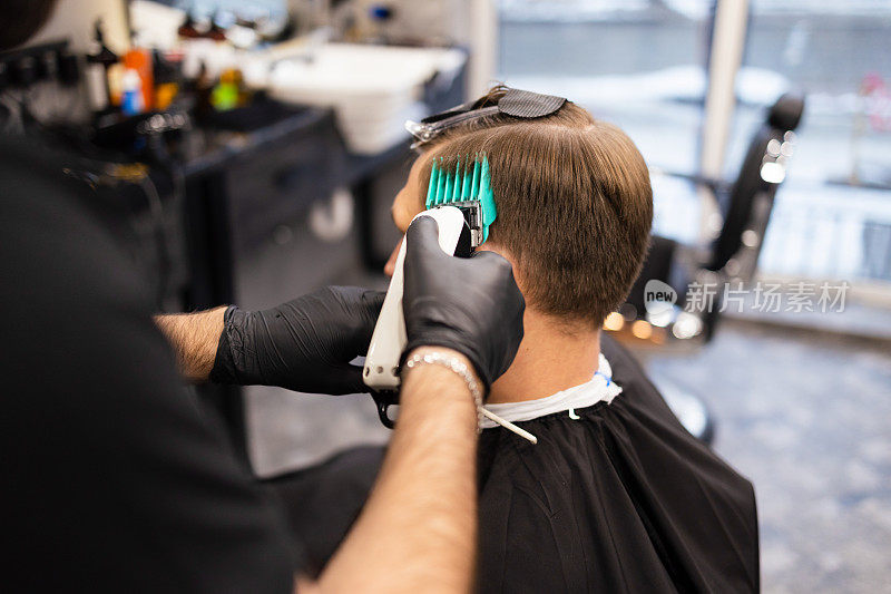理发师在理发店用发胶和梳子给头发定型。年轻英俊的白人男子在一个现代发廊理发