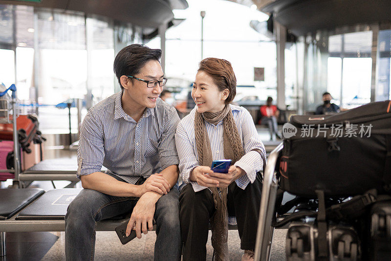 亚洲华人夫妇戴着口罩，在机场候机时用智能手机上网