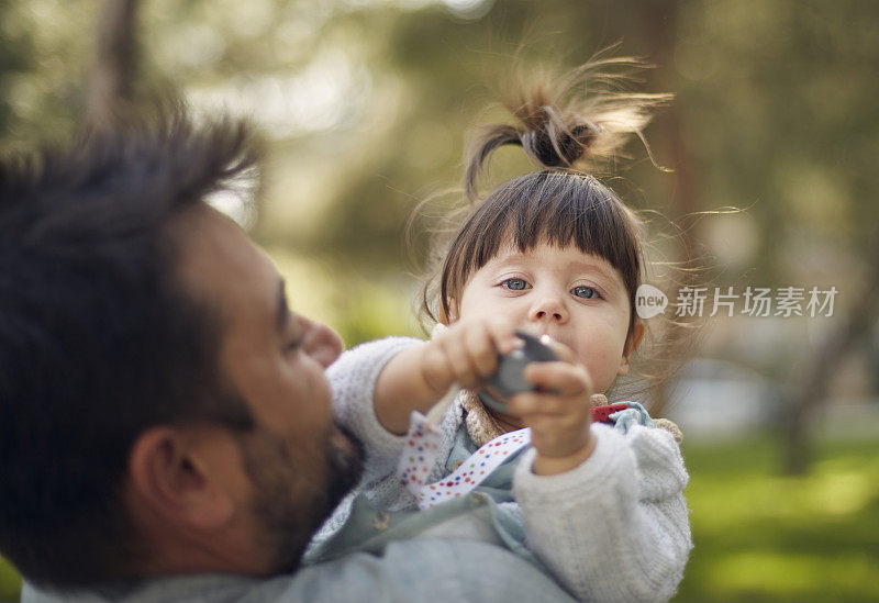 可爱漂亮的小女孩用奶嘴在她爸爸的腿上摆姿势拍照