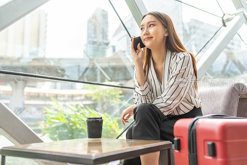 美丽的年轻亚洲女性商务独自女旅行者在机场候机楼的咖啡馆里等待起飞时用智能手机打电话