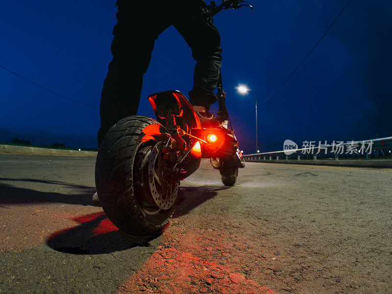 一个人骑着电动车在路上。夜晚的路，灯火通明。强大的现代化电动运输，后视镜
