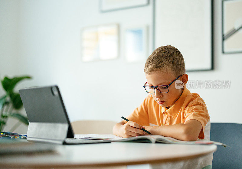 严肃男孩在家一边用电子平板电脑一边做作业