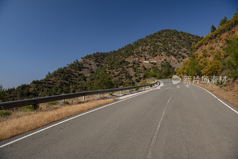 道路拥抱着蜿蜒的山坡，越过遥远的山峰，在森林稀疏的山上攀爬陡峭的火山地形