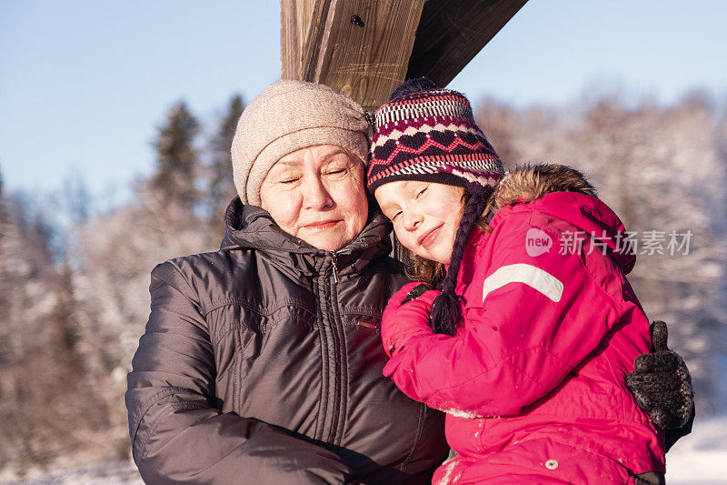 孩子亲切地拥抱着他的祖母。一个77岁的老妇人和一个7岁的女孩在冬天散步。