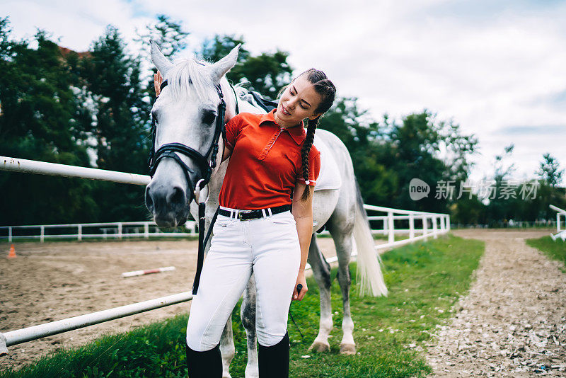 穿着休闲服装的白人妇女在农场围场骑马休闲时拍马，年轻的女骑师照顾纯种马冠军种马
