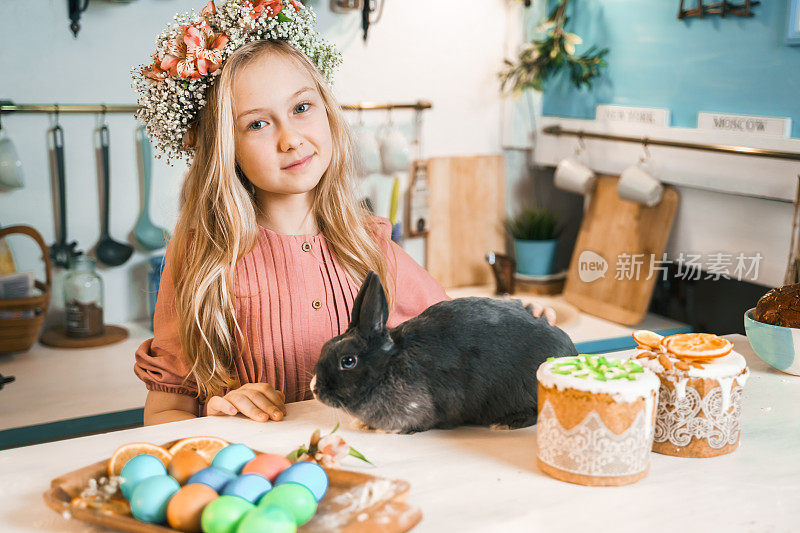 美丽的女孩头戴花环庆祝复活节。做蛋糕，在餐桌上画鸡蛋。节日快乐在一起。和复活节兔子玩，兔子