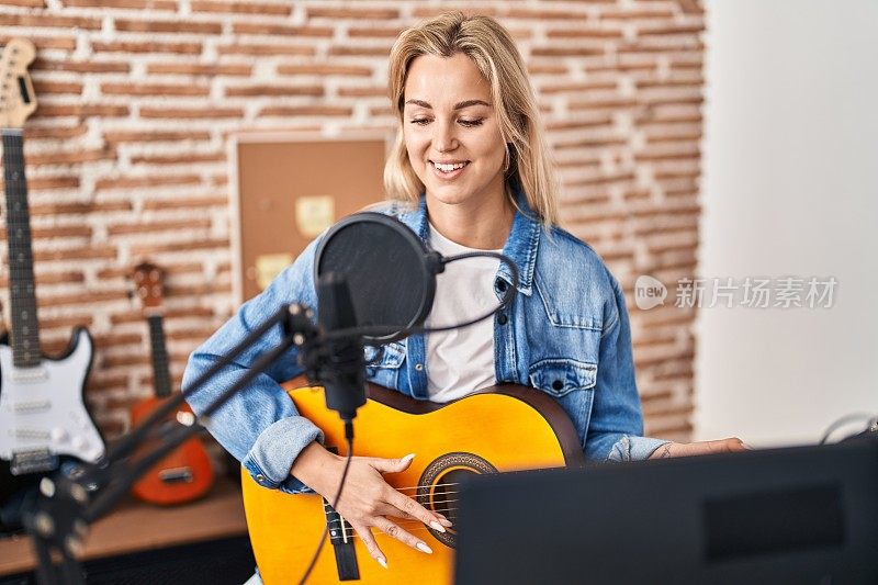 年轻的金发女音乐家唱着歌，在音乐工作室弹奏西班牙吉他
