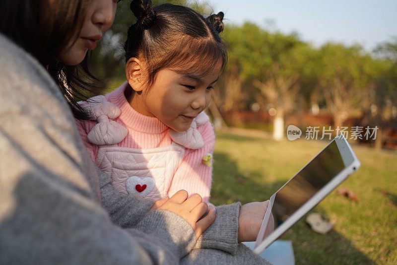 可爱的亚洲小女孩和她的妈妈玩平板电脑