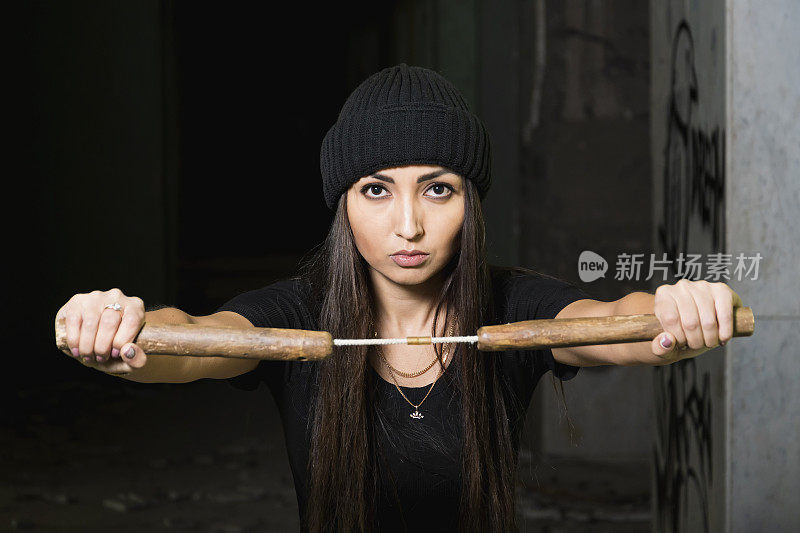 一个年轻女孩，黑发，穿着运动服准备战斗。中国武器——双节棍