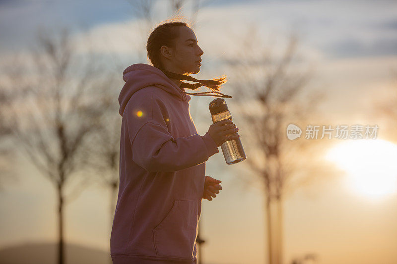 日落时分，一名年轻女子在公园慢跑时补水。