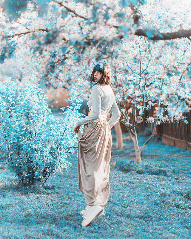 染蓝头发的亚洲女人，背景是春天的树。爆炸的发型。花园。白色的花朵