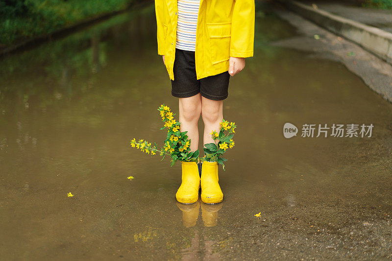 春天的一天，可爱的小男孩穿着雨衣和胶靴走过水坑