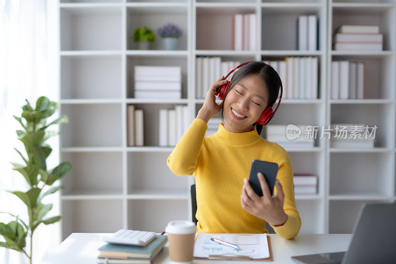 快乐的年轻亚洲女学生戴着耳机在手机上听音乐。