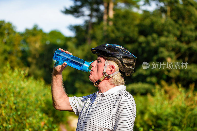 在森林小道上，骑自行车的年长男性正在用水瓶喝水