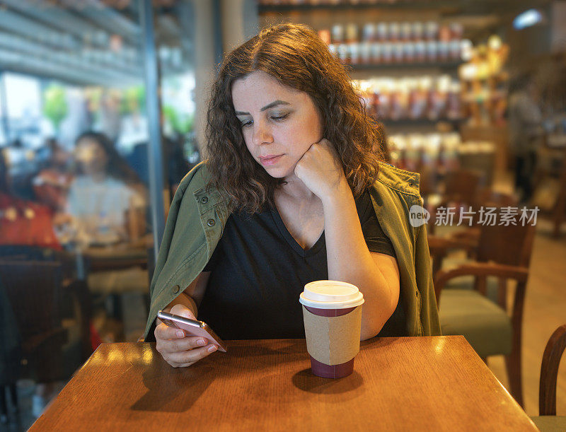 美女一边在咖啡店喝咖啡，一边用智能手机做金融工作。复古色调。