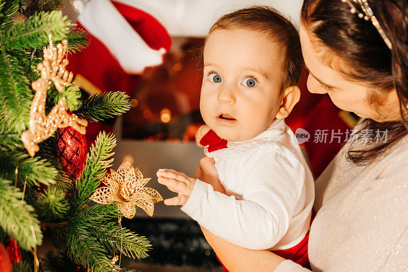 母亲和她的孩子在圣诞树旁庆祝。一位美丽的年轻母亲抱着她的小儿子，他们紧紧地拥抱在一起。圣诞图片，树和灯的背景。