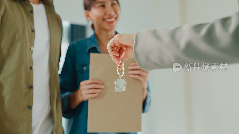 签约后，年轻的亚洲女性房地产经纪人将房子钥匙交给客户的特写。买新房子。