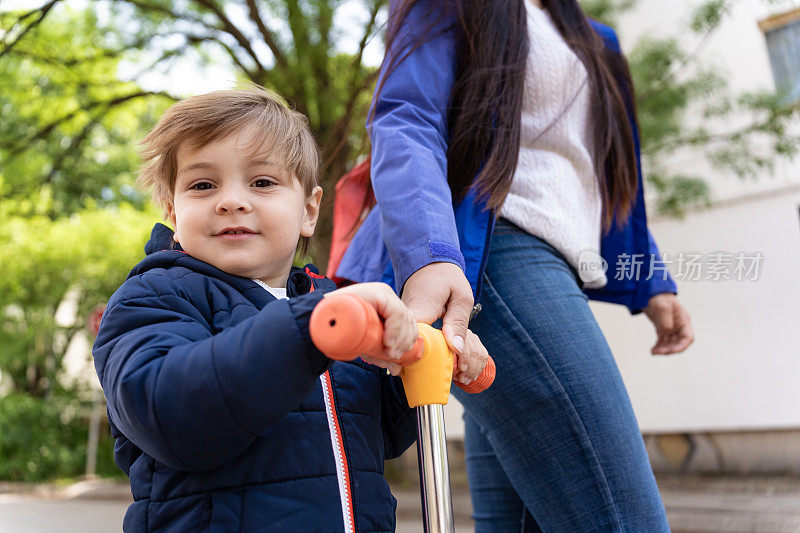 一个蹒跚学步的孩子骑着摩托车，他的妈妈在旁边