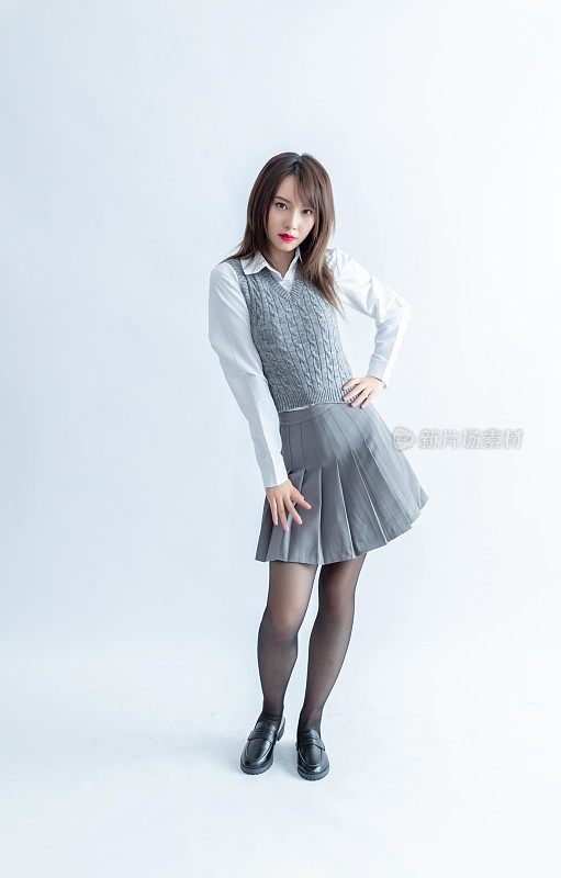 一位身穿灰色百褶裙和白色衬衫的年轻亚洲女子自信地摆姿势，双手叉腰。