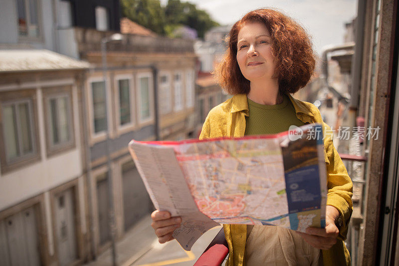 好奇的资深女性站在阳光明媚的阳台上探索城市地图