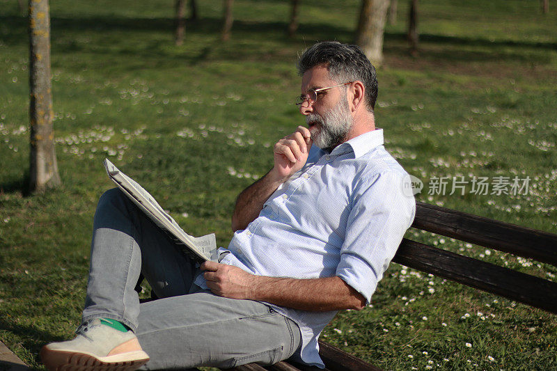 成熟的男人在公园里看报纸