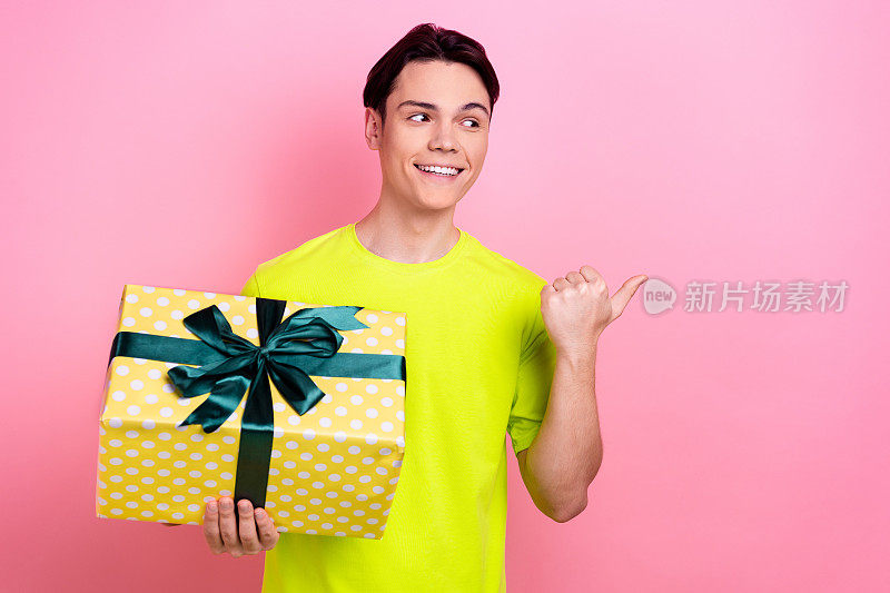 照片肖像英俊的少年男子拿着礼物盒点空的空间穿着时髦的黄色服装孤立在粉红色的背景
