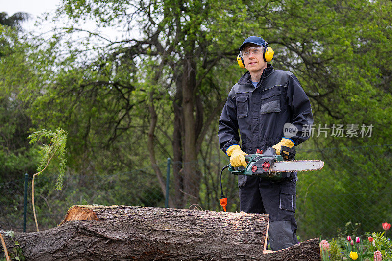 一个穿制服的人正在院子里用电锯锯一棵老树。