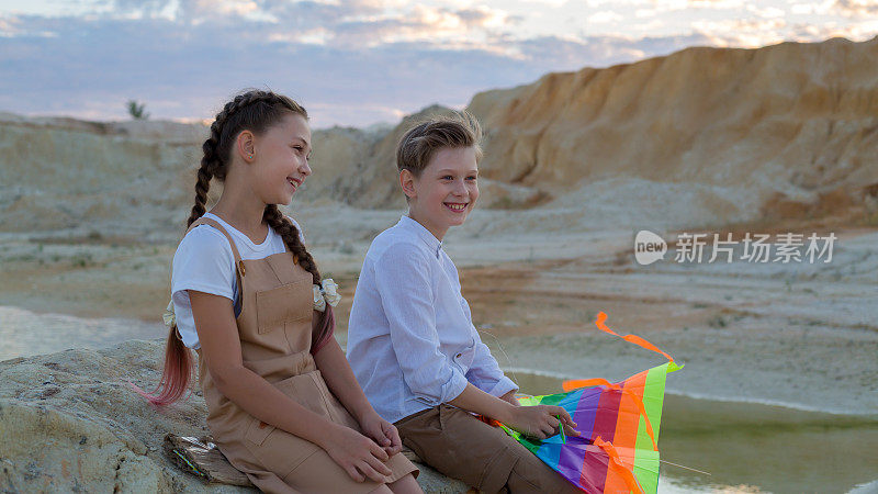 一个8-9岁的男孩和一个8-9岁的女孩拿着风筝在山上聊天