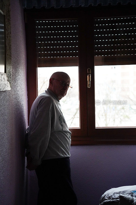 一个老人在他的卧室里看着窗外。老年孤独