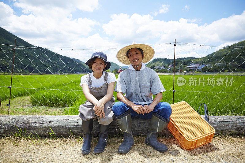 微笑的男人和女人坐在稻田前的圆木上