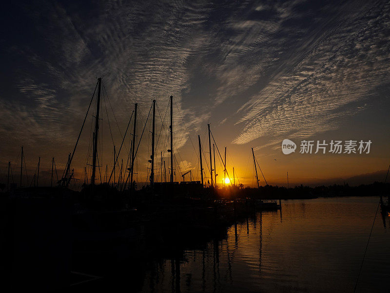 帆船的剪影，在日出时停泊在平静的港口。