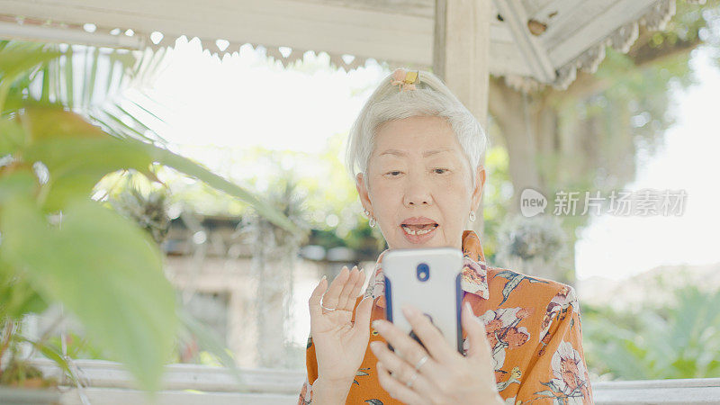 在户外使用智能手机视频通话的亚洲老年妇女，银发上网者，积极拥抱科技的老年妇女