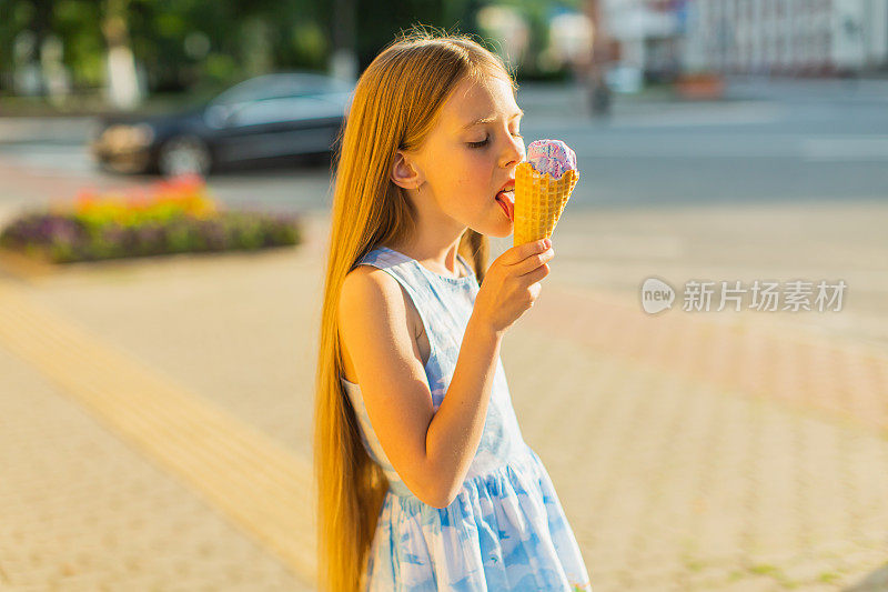 穿蓝裙子的金发女孩在吃冰淇淋。夏天的生活方式。童年