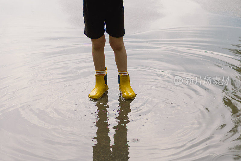 春天的一天，可爱的小男孩穿着雨衣和胶靴走过水坑