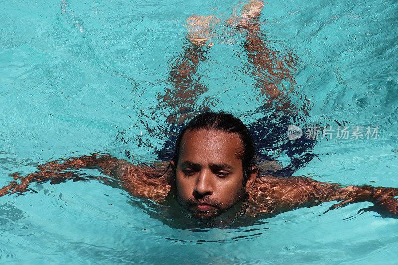 全画幅印度男子在清澈的水中做蛙泳，室外，游泳池，绿松石蓝色马赛克瓷砖被波纹水扭曲，游泳和飞溅，波涛起伏的水面反射，重点放在前景