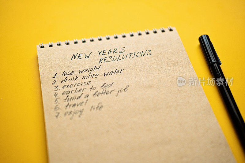 新年决心，2023年的目标，在黄色桌面背景的开放式记事本中列出改善生活的决心。开始新的生活，计划和设定目标