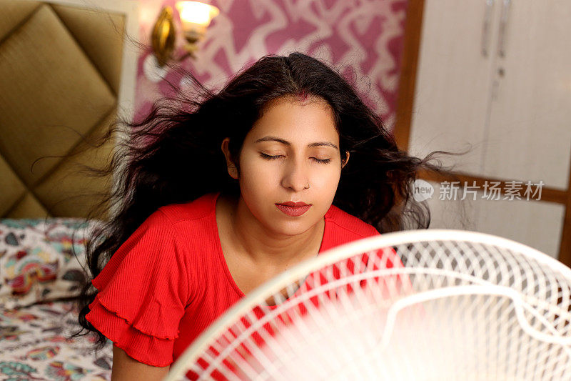 年轻的印度妇女用扇子吹干她潮湿的头发