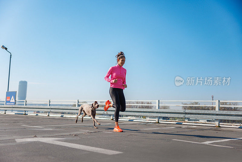 在晴朗的天空下，一个活跃的女人带着她的狗在空荡荡的停车场里跑步