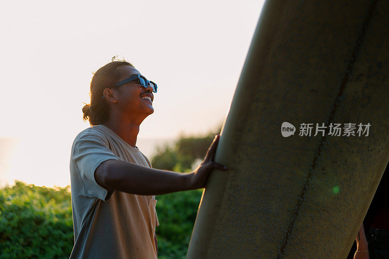 夕阳下，印尼男冲浪者看着他的冲浪板